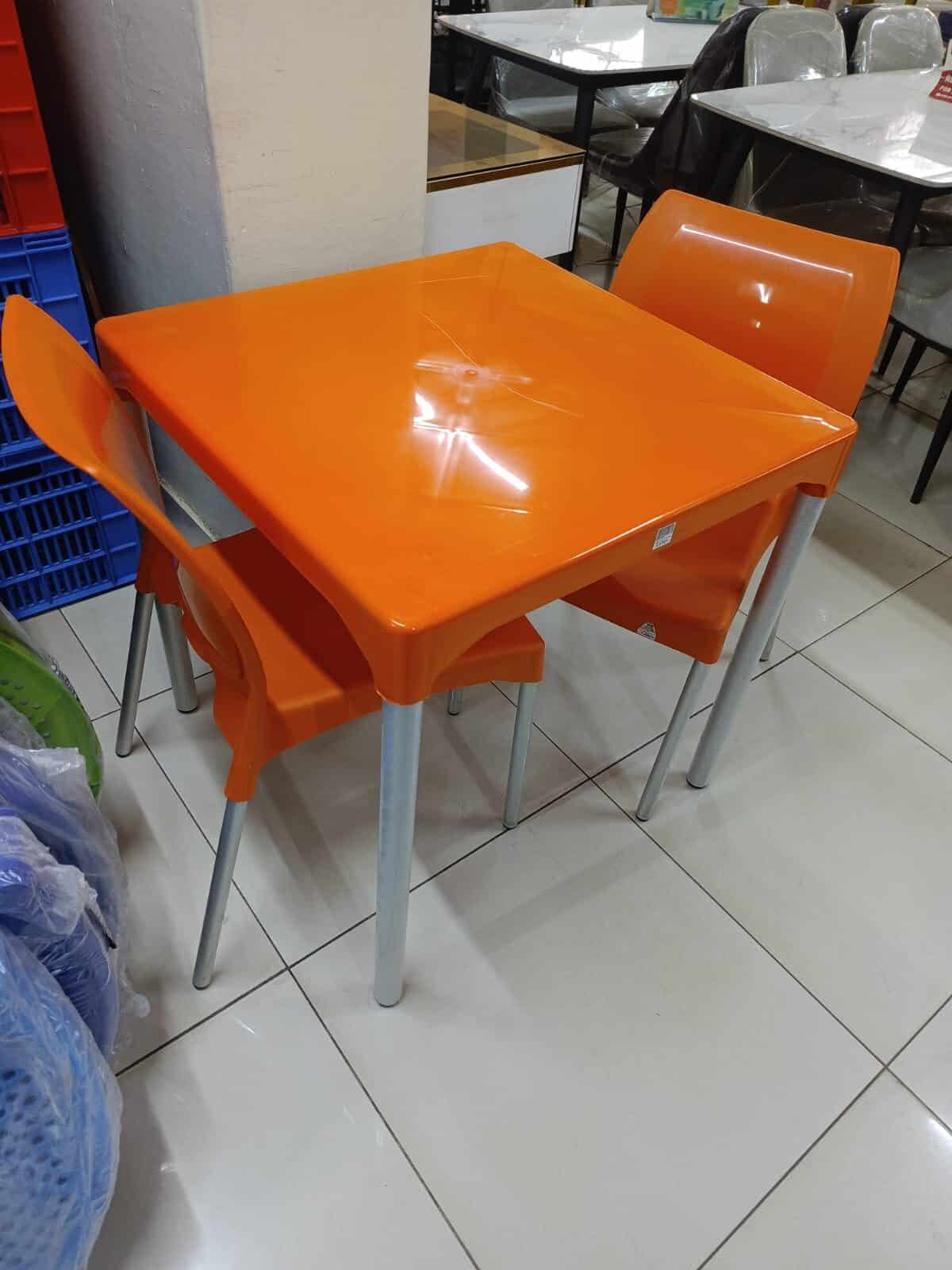 Orange plastic table and chairs set for kitchen or dining area, ideal for home or restaurant use, lightweight and durable, perfect for small spaces or kids' dining zones.